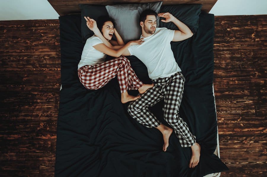 couple lying in bed while woman kick his husband